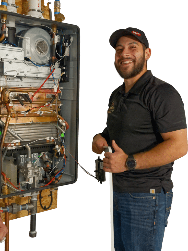 A technician stands next to a detailed panel of plumbing and heating equipment, including wires and components, while holding a tool. The technician wears a black shirt and has a beard, smiling while looking toward the camera.