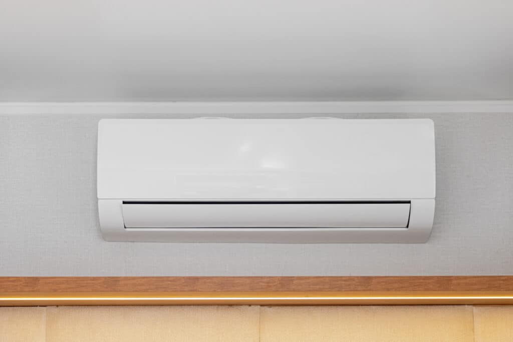 A white wall-mounted air conditioning unit is installed near the ceiling. The unit has a sleek design with a horizontal air vent and is positioned against a light gray wall.